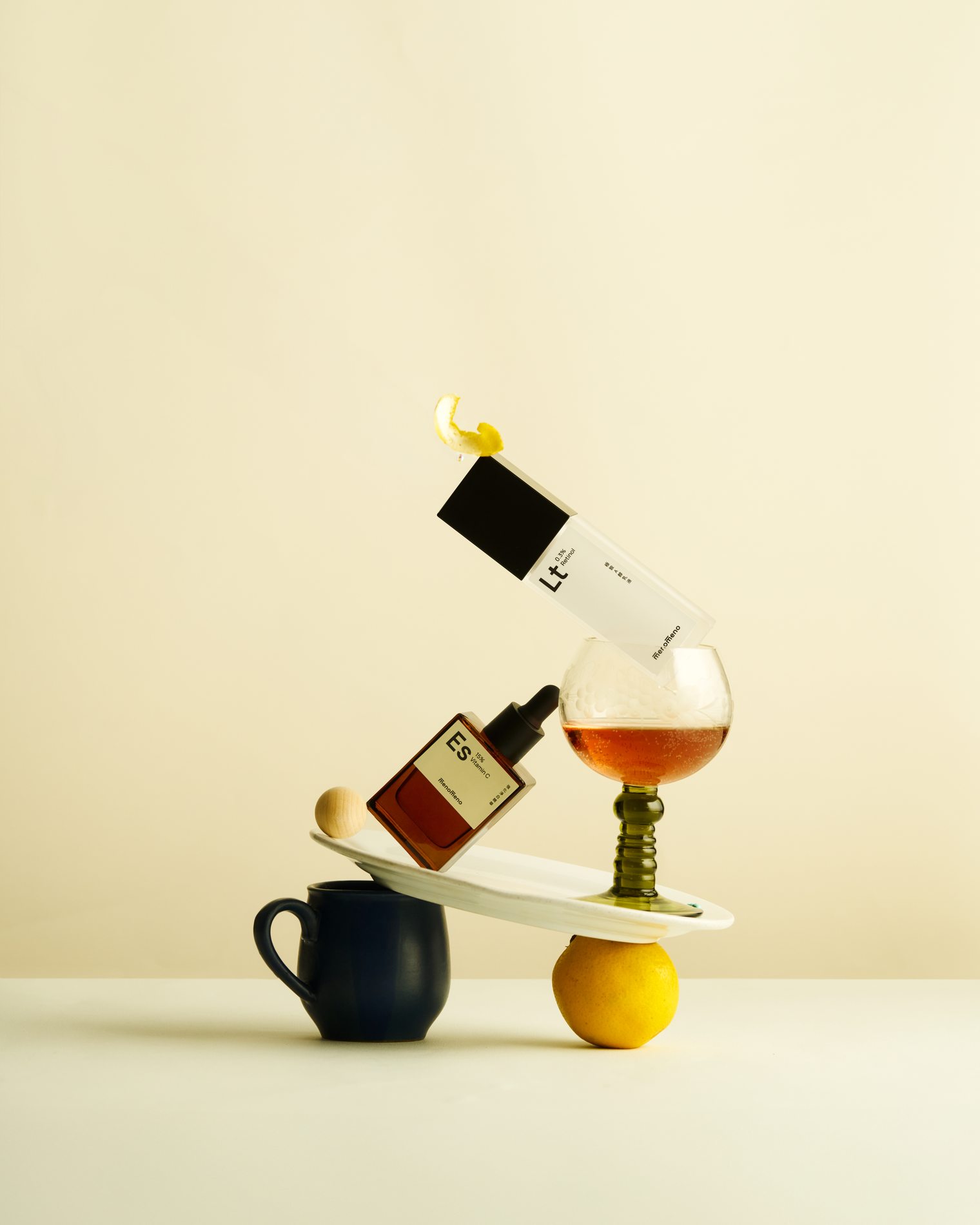 淺黃色背景中,保養品瓶身與玻璃杯、果實及小型器物形成平衡構圖