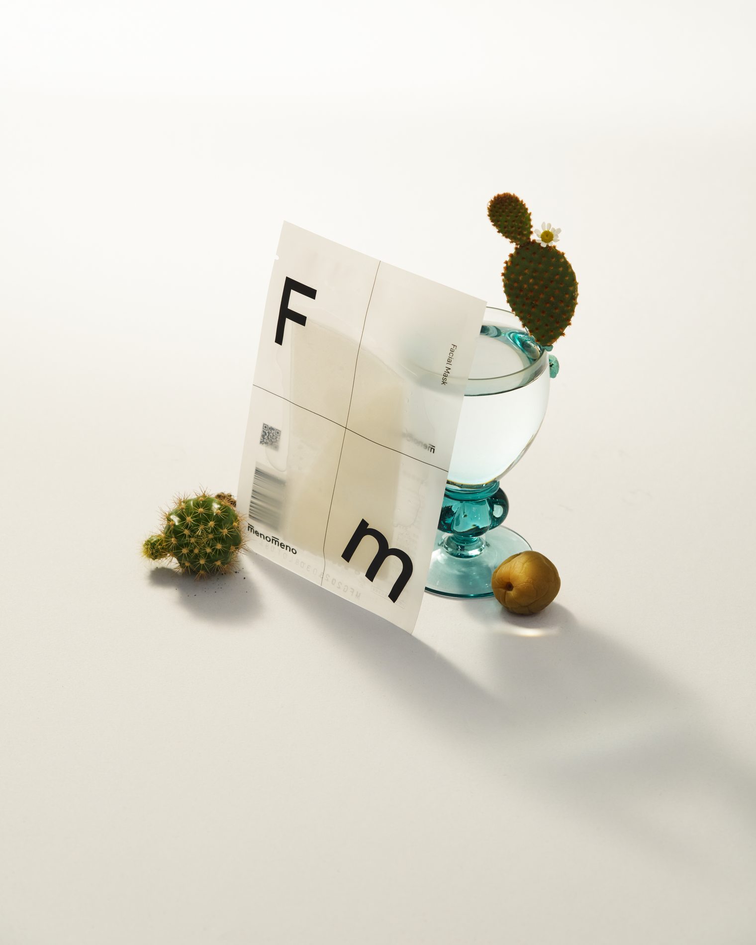 半透明包材、玻璃杯與小型植物組成的白色靜物畫面