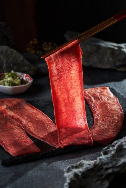 筷子夾起一片肉,深色石材與肉品紋理形成對比