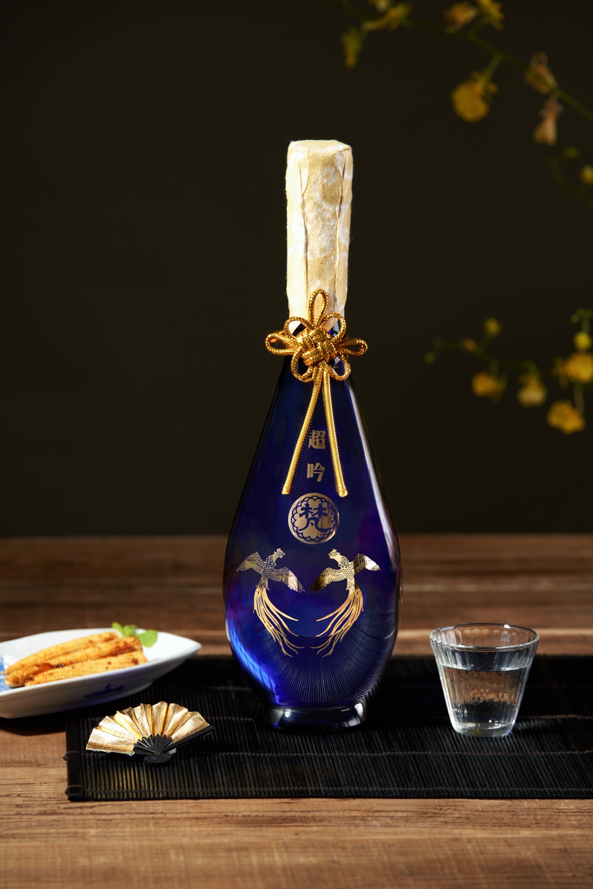深色背景中的藍色酒瓶、清酒杯與小食