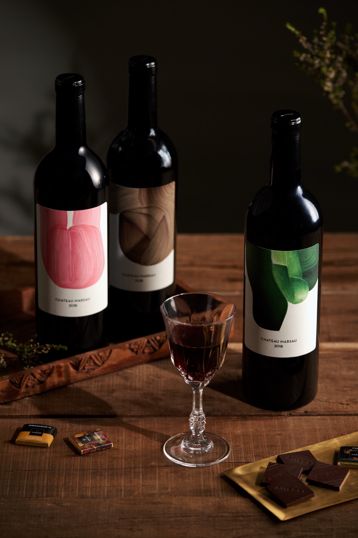木桌上的三瓶葡萄酒、酒杯與巧克力