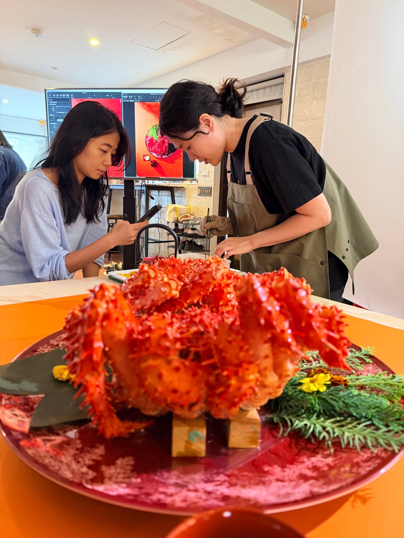 食物造型團隊在橘色桌面整理蟹類,後方螢幕顯示攝影畫面